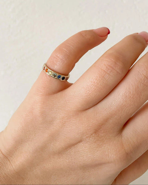 A gold ring with a glossy polished surface, featuring a series of colorful gemstones set in a row worn as a pinky ring.